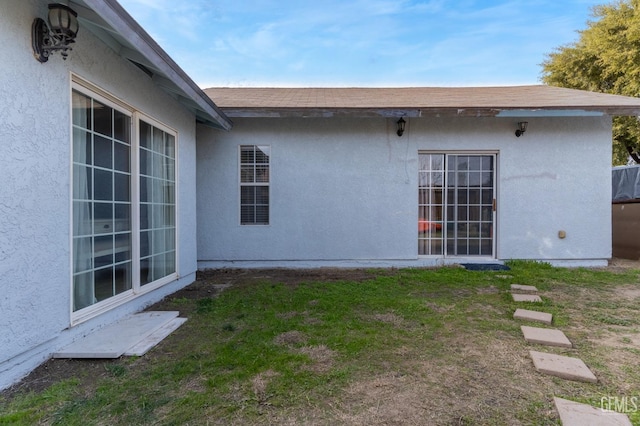 exterior space featuring a yard, roof with shingles, and stucco siding