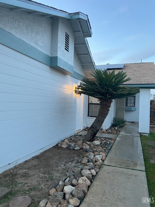 view of side of home with solar panels and roof with shingles