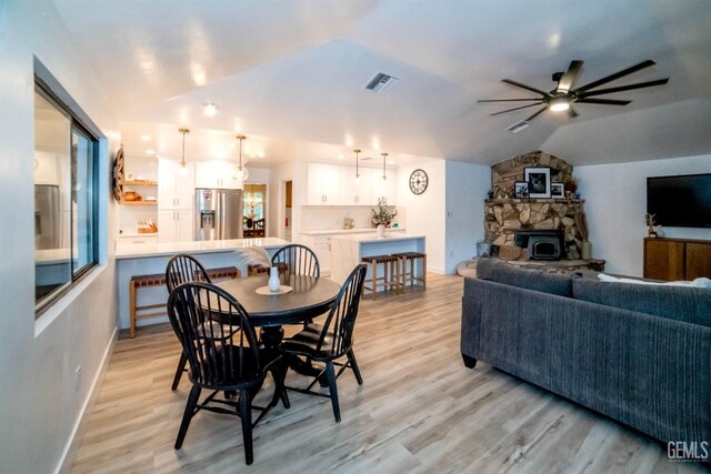 dining space featuring light hardwood / wood-style floors, vaulted ceiling, ceiling fan, and a stone fireplace