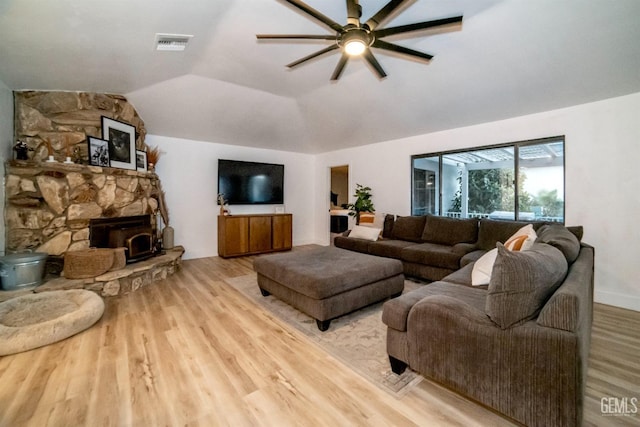 living room with a wood stove, light wood-type flooring, vaulted ceiling, and ceiling fan