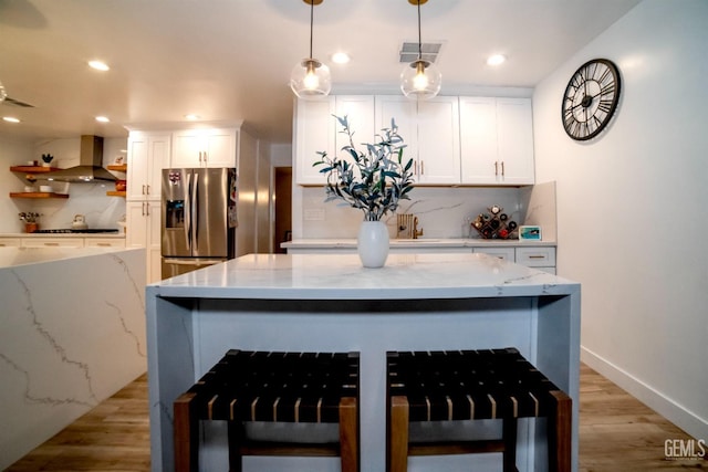 kitchen with stainless steel fridge with ice dispenser, pendant lighting, white cabinetry, and wall chimney range hood