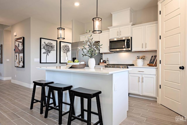 kitchen with decorative light fixtures, stainless steel appliances, white cabinets, and a center island with sink