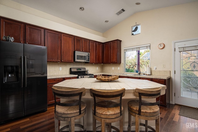 kitchen with lofted ceiling, appliances with stainless steel finishes, tile counters, a kitchen island, and decorative backsplash