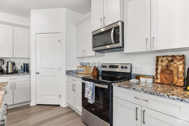 kitchen featuring white cabinets, appliances with stainless steel finishes, light wood-type flooring, and light stone countertops