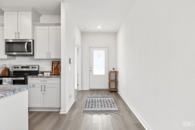 kitchen featuring light stone counters, white cabinetry, stainless steel appliances, light wood finished floors, and baseboards