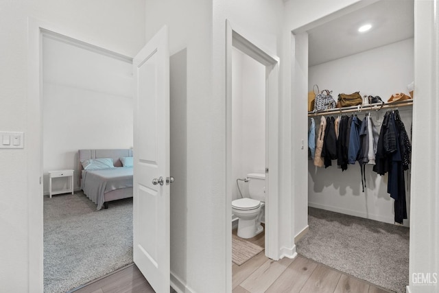 bathroom featuring toilet, a walk in closet, baseboards, and wood finished floors