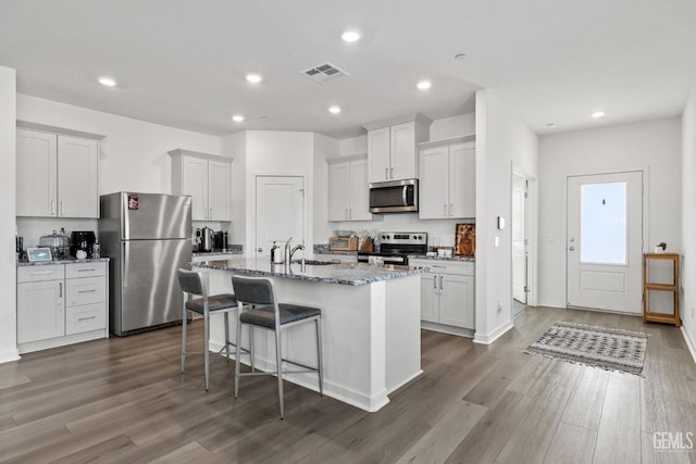 kitchen with light stone counters, a center island with sink, a breakfast bar, a sink, and stainless steel appliances