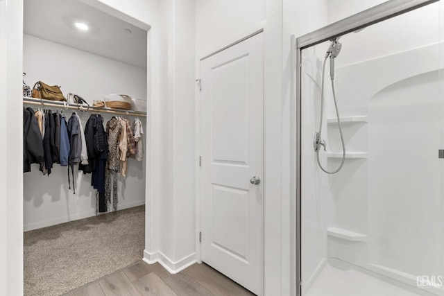 bathroom with a walk in closet, baseboards, wood finished floors, and a shower stall