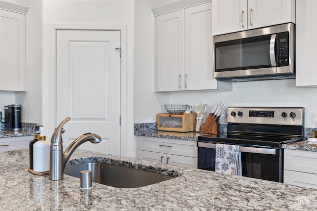 kitchen with light stone countertops, appliances with stainless steel finishes, white cabinetry, and a sink