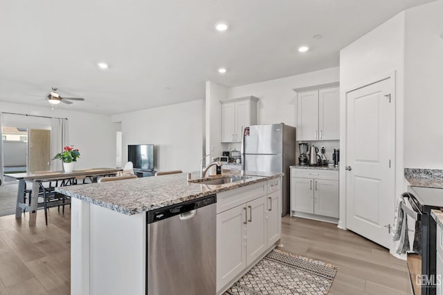 kitchen featuring light wood-type flooring, an island with sink, a sink, appliances with stainless steel finishes, and ceiling fan