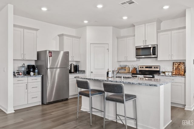 kitchen featuring a center island with sink, visible vents, appliances with stainless steel finishes, and wood finished floors