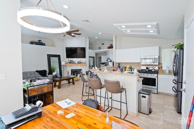 7519 Shadow Wells St, Bakersfield, CA 93313 - kitchen featuring stainless steel appliances, a breakfast bar, white cabinets, decorative backsplash, and a glass covered fireplace