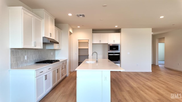 12801 Kinnick Ct, Bakersfield, CA 93311 - kitchen featuring light wood-type flooring, black oven, decorative backsplash, a center island with sink, and recessed lighting