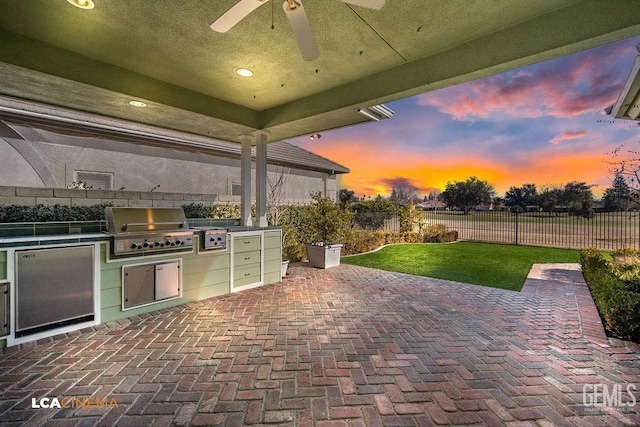 patio terrace at dusk featuring ceiling fan, an outdoor kitchen, and grilling area