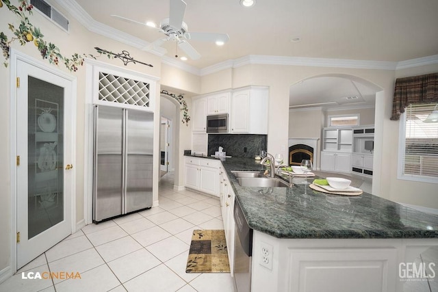 kitchen with sink, white cabinetry, built in appliances, light tile patterned floors, and ornamental molding