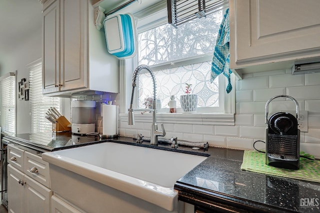 kitchen with a sink, dark countertops, white cabinetry, and backsplash