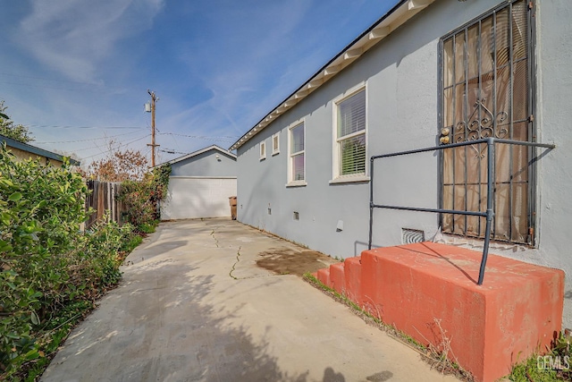 view of property exterior with a garage, an outbuilding, fence, and stucco siding