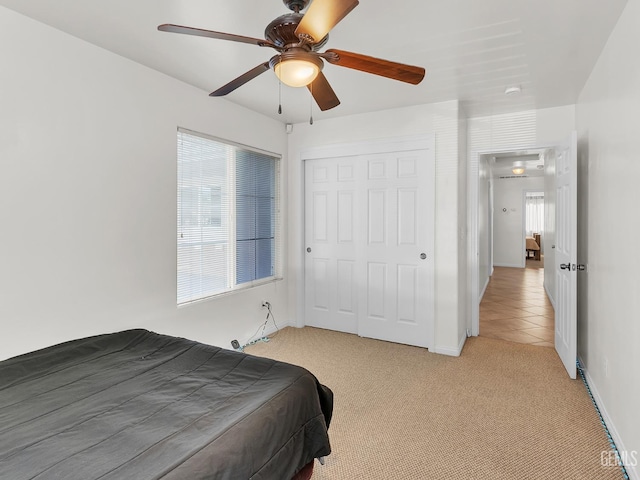 bedroom with a closet, ceiling fan, light carpet, and baseboards