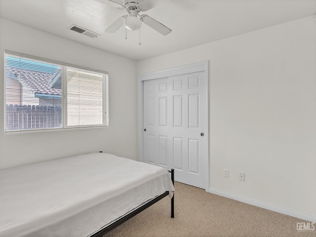 bedroom with a closet, ceiling fan, visible vents, baseboards, and light colored carpet