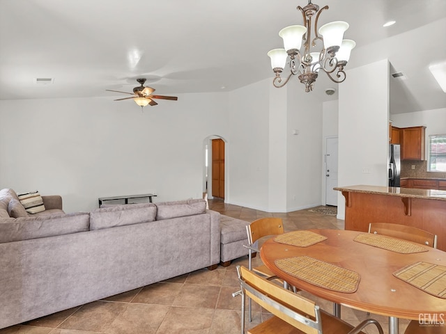 dining room with arched walkways, light tile patterned floors, vaulted ceiling, ceiling fan with notable chandelier, and visible vents