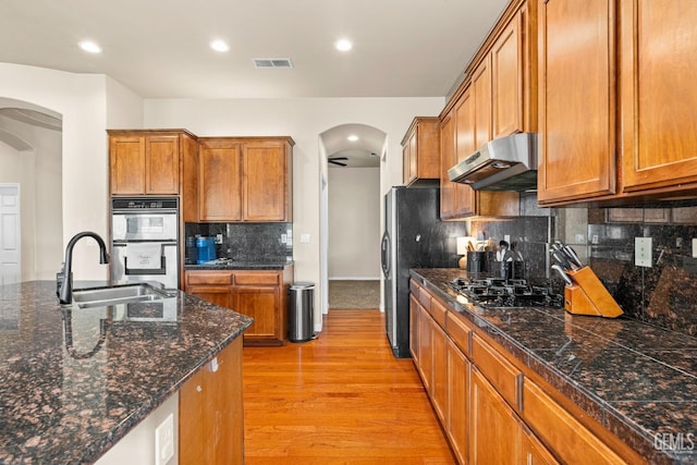 9310 Via Catania, Bakersfield, CA 93312 - kitchen featuring stainless steel appliances, under cabinet range hood, light wood-style floors, brown cabinetry, and arched walkways