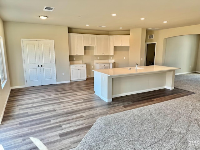 kitchen featuring white cabinets, light wood-type flooring, sink, and an island with sink