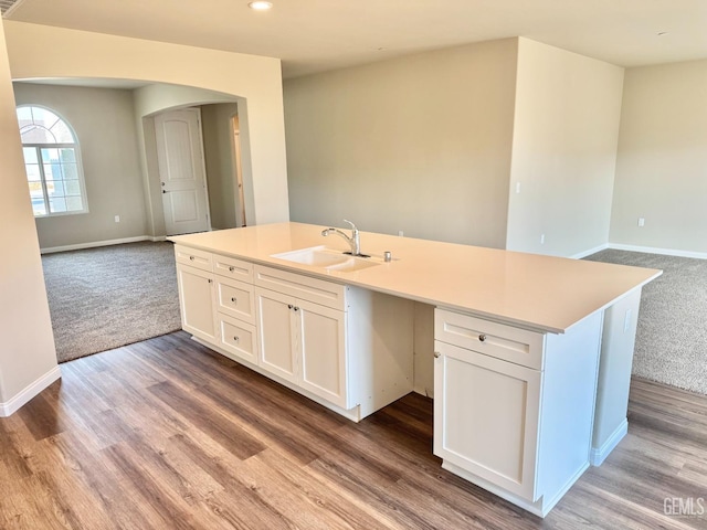 kitchen featuring sink, an island with sink, white cabinets, built in desk, and light wood-type flooring