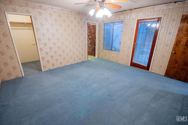 unfurnished bedroom featuring carpet floors, wallpapered walls, a walk in closet, and a textured ceiling