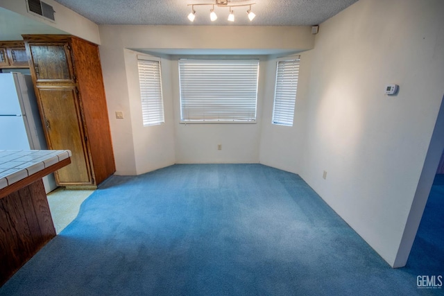 unfurnished dining area featuring a textured ceiling, light carpet, and visible vents