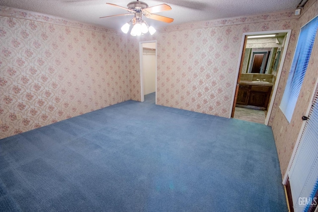 carpeted spare room featuring a textured ceiling, a sink, a ceiling fan, and wallpapered walls