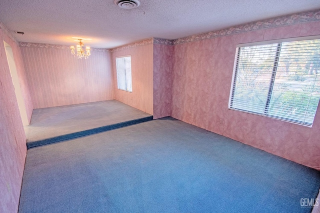 carpeted empty room featuring a textured ceiling, plenty of natural light, a chandelier, and visible vents