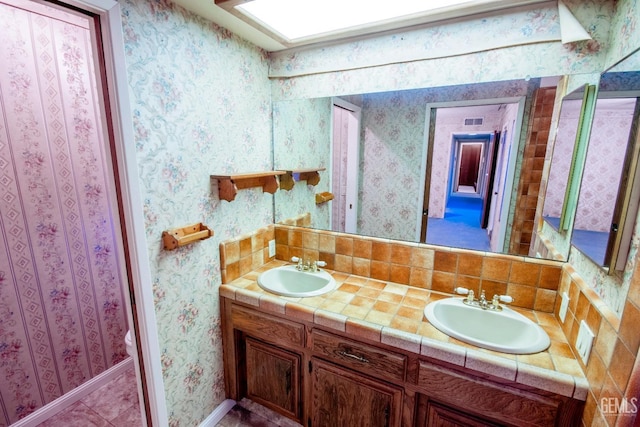 full bath featuring double vanity, wallpapered walls, and a sink