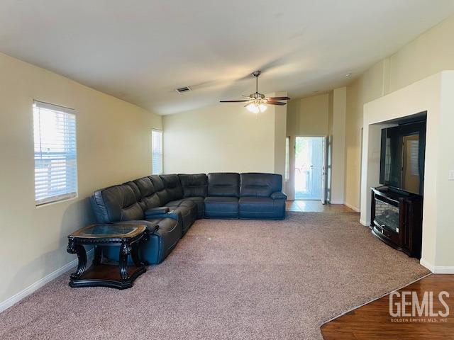 carpeted living room with a ceiling fan, baseboards, visible vents, and vaulted ceiling