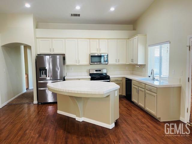 kitchen with visible vents, a sink, a kitchen island, arched walkways, and appliances with stainless steel finishes