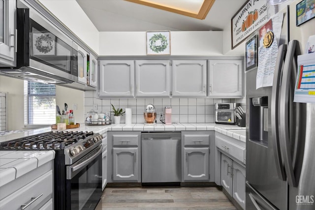 6305 Wolfe Creek Dr, Bakersfield, CA 93306 - kitchen featuring stainless steel appliances, gray cabinetry, tile counters, and light wood-style flooring