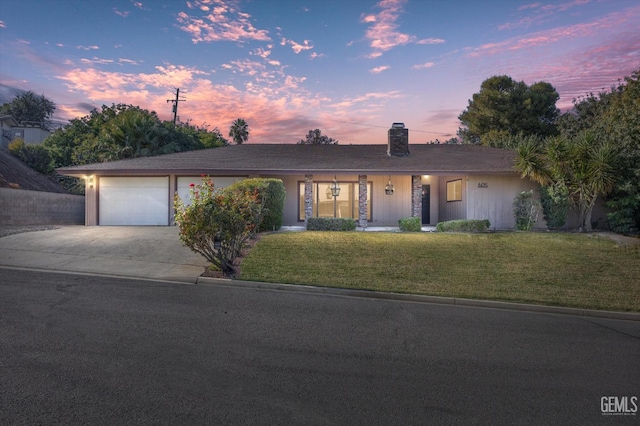 ranch-style house featuring driveway, a garage, a chimney, and a lawn