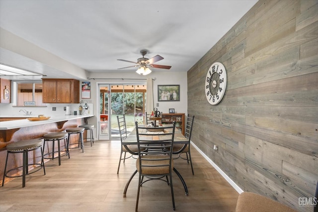 dining space with light wood-type flooring, wood walls, ceiling fan, and baseboards