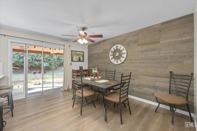 dining area with light wood-type flooring, wood walls, baseboards, and a ceiling fan