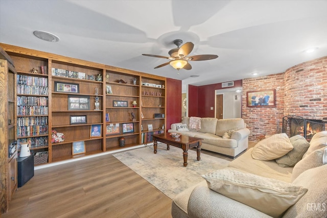 living room featuring visible vents, a ceiling fan, brick wall, wood finished floors, and a brick fireplace