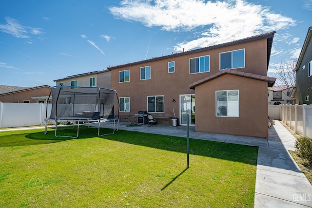 back of house featuring a trampoline, a lawn, and a patio area