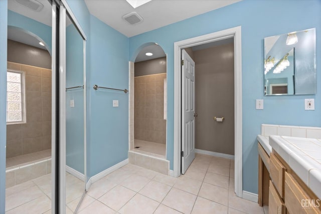 bathroom with a tile shower, vanity, and tile patterned flooring