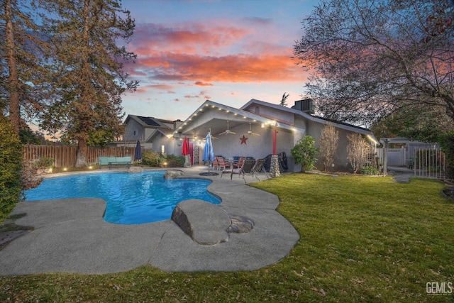 pool at dusk featuring a patio, ceiling fan, and a yard