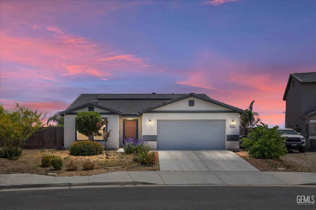 10028 Fire Island Dr, Bakersfield, CA 93313 - ranch-style home featuring a garage, driveway, roof mounted solar panels, stucco siding, and a tiled roof
