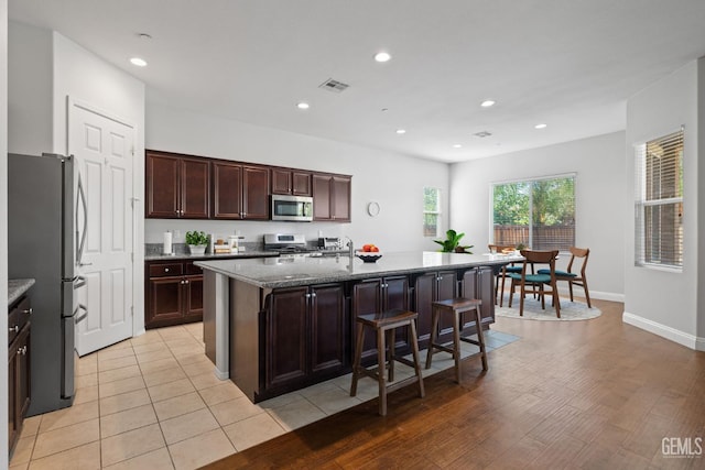 9904 Toscana Dr, Bakersfield, CA 93306 - kitchen with appliances with stainless steel finishes, dark stone countertops, a kitchen island with sink, recessed lighting, and a breakfast bar area
