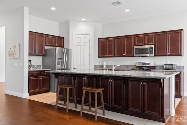 9904 Toscana Dr, Bakersfield, CA 93306 - kitchen with stainless steel appliances, light wood-style floors, a center island with sink, stone countertops, and recessed lighting