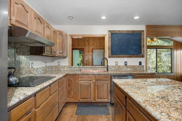 kitchen with dishwasher, sink, light wood-type flooring, light stone counters, and black electric cooktop