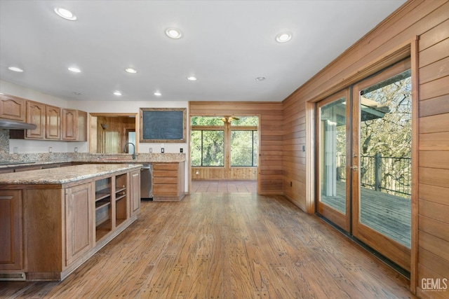 kitchen with wood walls, light stone counters, black electric cooktop, dishwasher, and light hardwood / wood-style floors