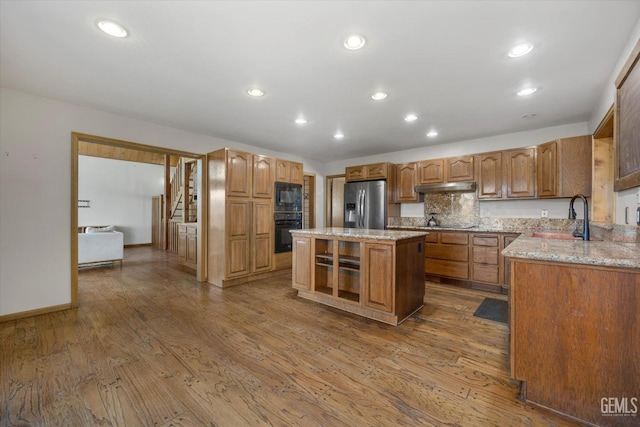 kitchen featuring sink, a center island, hardwood / wood-style flooring, light stone countertops, and black appliances