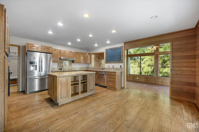 kitchen with wood walls, light stone counters, a center island, light hardwood / wood-style flooring, and stainless steel appliances