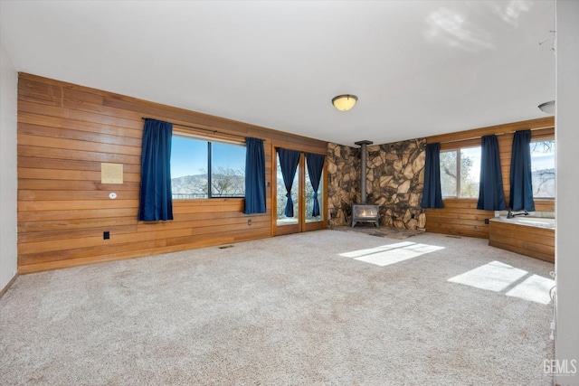 unfurnished living room featuring wood walls, carpet, and a wood stove